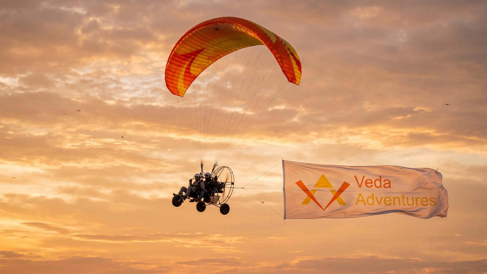 Veda Adventures banner flying behind a powered paraglider at sunset